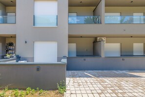 A modern multi-story residential building with balconies, a covered outdoor area, and a paved walkway. - The Oak Haven (Split)