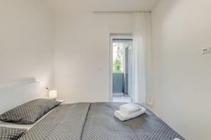 Ein Schlafzimmer mit einem Bett, einem Nachttisch, einer Lampe und Blick ins Freie.