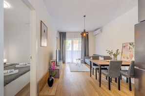 A modern living room with a sofa, dining table, chairs, a small side table with a vase, and a picture frame. - The Oak Haven (Split)