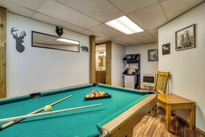 Une table de billard avec des billes, une chaise en bois et des décorations murales comprenant des silhouettes d’animaux et un ours.