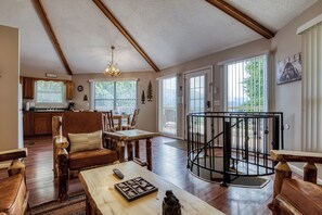 A spacious living area with a wooden floor, a dining table, and a staircase with a black railing. - Octagon Chalet: Hot Tub, Pool Table & Stunning Mountain Views - Sleeps 6 (Gatlinburg)