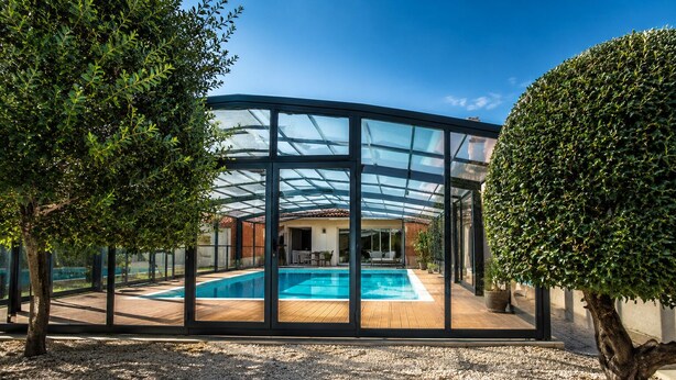 A modern house with a glass-enclosed swimming pool, surrounded by gravel and trees. - Family home in secure residence with swimming pools close to beaches (Béziers)