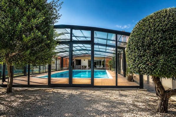 A modern house with a glass-enclosed swimming pool, surrounded by gravel and trees. - Family home in secure residence with swimming pools close to beaches (Béziers)