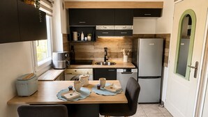 A compact kitchen with modern appliances, a dining area with two chairs, and a view of the outdoors through a window. - Family home in secure residence with swimming pools close to beaches (Béziers)