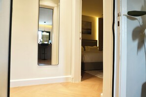 A hotel room with a wooden floor, a bed with white bedding, a bedside table, and a mirror on the wall. - The Lounge I Luxury 1BR with Private Bar I Almalqa (Riyadh)