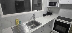 Una cuina amb un vàter d'acer inoxidable, un microones, un torrador i una placa de cocció.