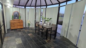 A covered patio area with a dining table and chairs, a wooden dresser, and potted plants. - Modern 2BR Home, Sleeps 5,  Parking,  Near Eastgate (Christchurch)