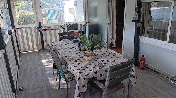 Ein Zimmer mit Tisch, der mit einer sternenmusternden Tischdecke bedeckt ist, einer Topfpflanze, einem Sessel, einem kleinen Beistelltisch und einem Feuerlöscher.