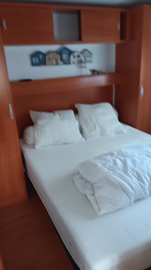 Ein Bett mit weißer Bettwäsche, einem Holzkopfstück und einem Regal darüber.