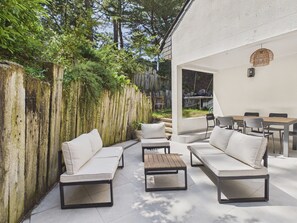Eine Terrasse im Freien mit Holzzaun, weißer Wand und einer Sitzecke mit Sofas und einem Tisch.