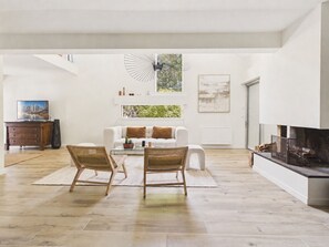 Ein großzügiges Wohnzimmer mit einem weißen Sofa, zwei Korbstühlen, einem Glastisch und einem Kamin.