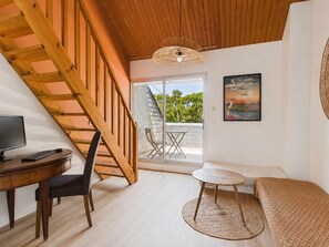 Ein Zimmer mit einer Holztreppe, einem Schreibtisch mit Computer, einer Couch, einem kleinen runden Tisch und einem Poster an der Wand.