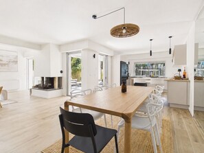 Eine moderne Küche mit weißen Schränken, eine Essecke mit einem Holztisch und Stühlen sowie ein großes Fenster mit Blick ins Freie.
