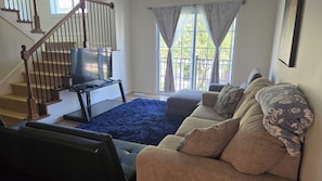 Ein Wohnzimmer mit Treppe, einem blauen Teppich, einer Couch und einem Fernseher auf einem Schrank.