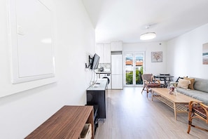 Eine moderne Küche mit weißen Schränken, ein Essbereich mit Holztisch und Stühlen sowie eine Wohnarea mit Sofa und Fernseher.