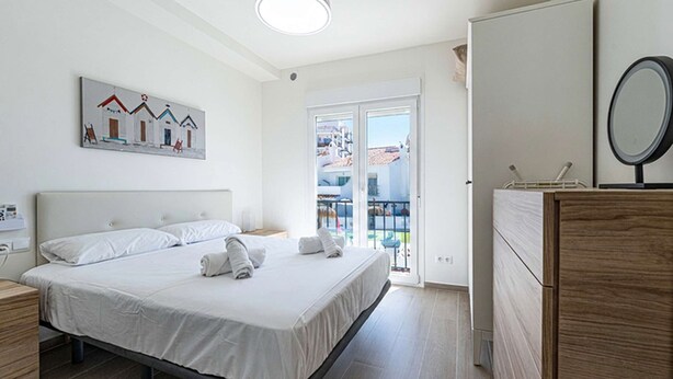 Quarto com cama, cômoda, espelho e varanda com vista.