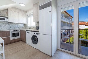 Eine moderne Küche mit integrierten Geräten, einer Waschmaschine und einer großen Schiebeglastür, die auf einen Balkon mit Gartenmöbeln führt.
