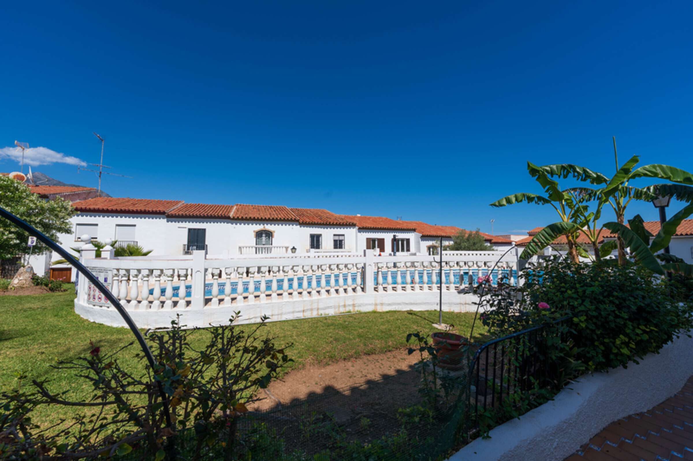 Un edifici de color blanc amb teules vermelles, envoltat per una tanca blanca, i un cel blau clar.