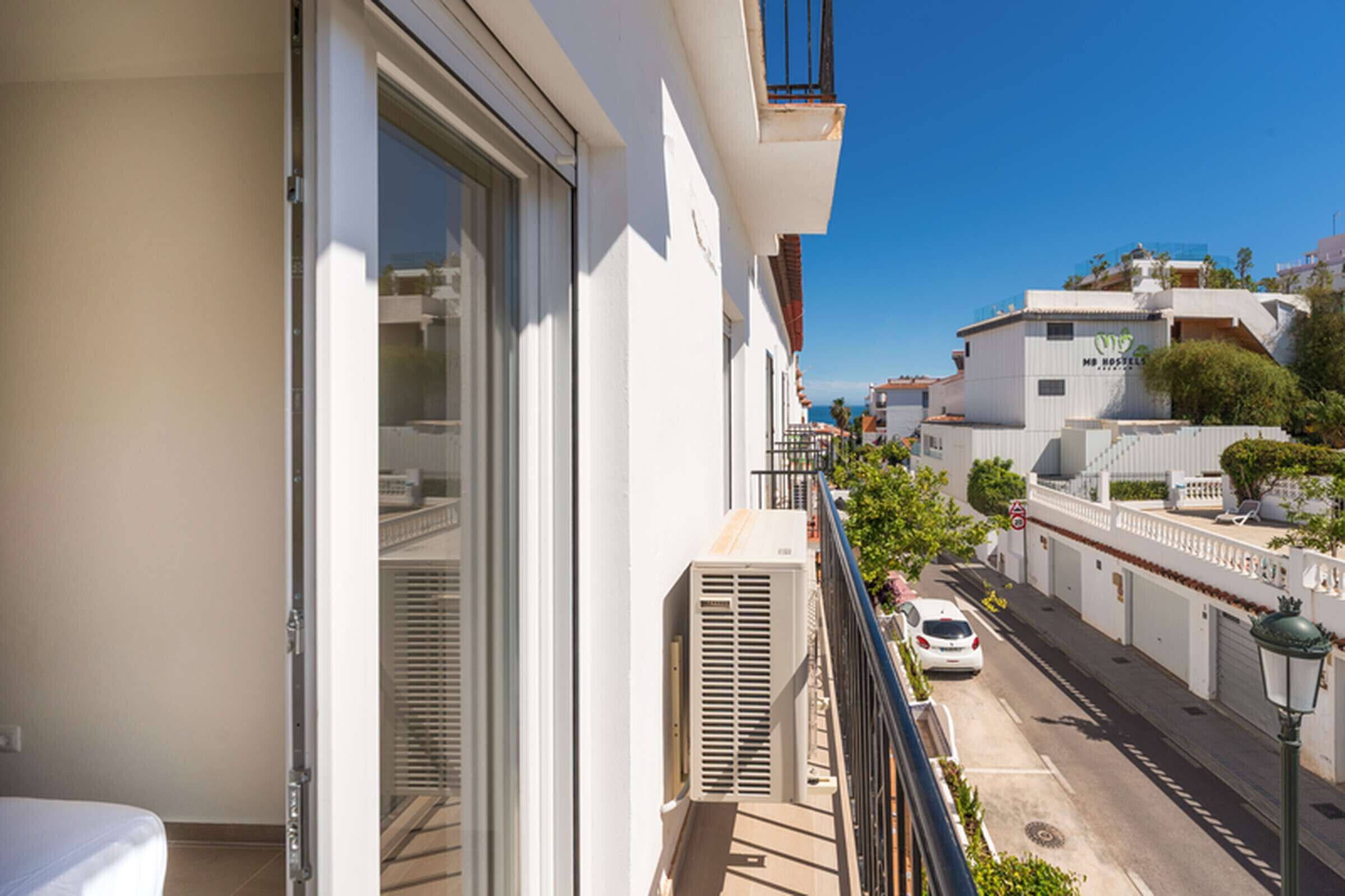 Un balcone con vista su una strada, un'auto bianca parcheggiata e un edificio con un cartello che indica 'MB Hostel'.