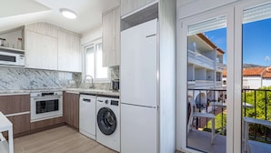 A modern kitchen with built-in appliances, a washing machine, and a large sliding glass door leading to a balcony with outdoor furniture. - Hacienda 4A by Casasol (Nerja)