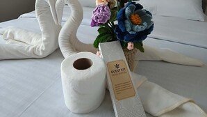 A neatly made bed with white linens, a swan-shaped pillow, a rolled-up towel, a floral arrangement, and a guest kit box. - Cozy condo Near Roxas Night Market (Davao City)