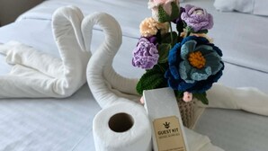 A bed with a white blanket, a swan-shaped towel, a bouquet of crocheted flowers, and a 'Guest Kit' box. - Cozy condo Near Roxas Night Market (Davao City)