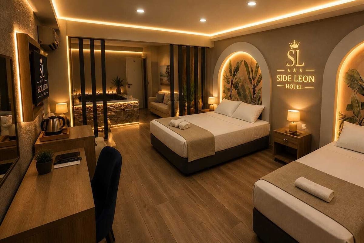 A hotel room with two beds, a desk, a chair, a small table, and a wall-mounted TV.