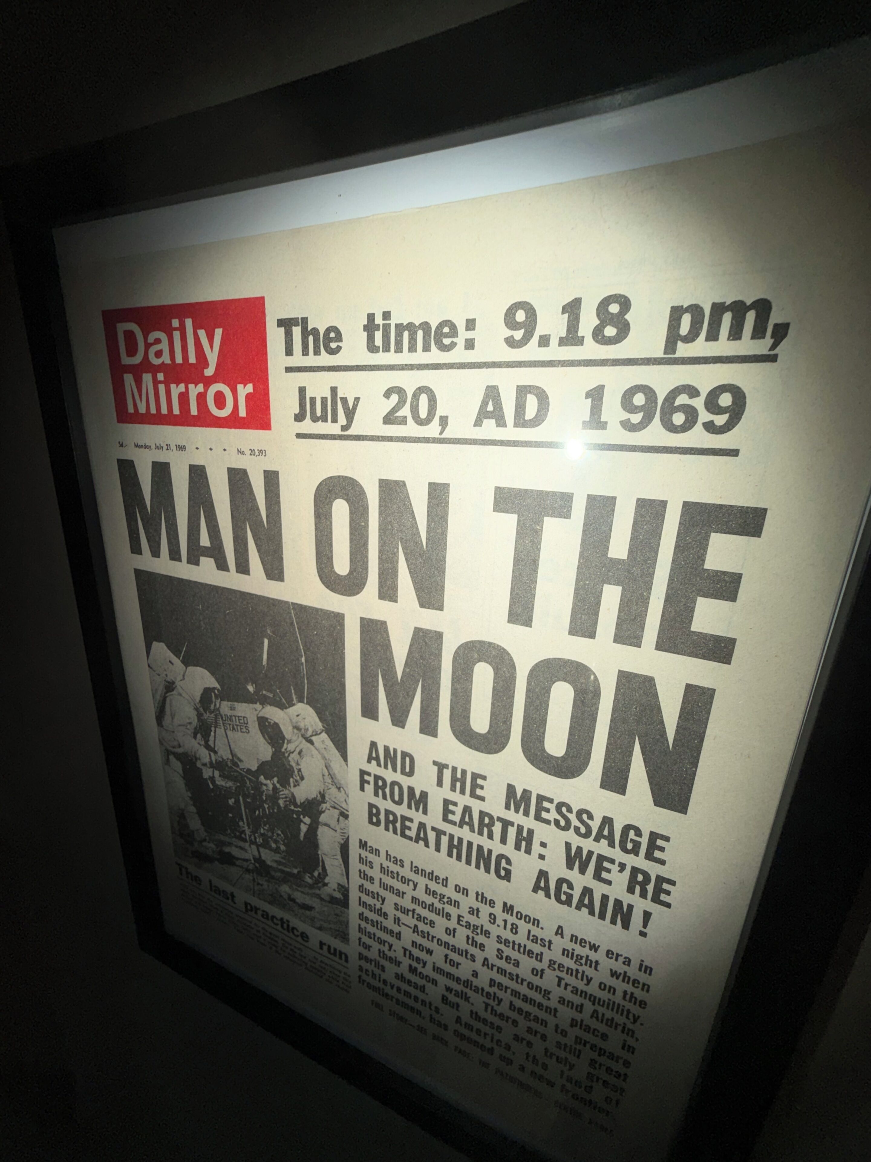 Un article de journal encadré, intitulé « L’HOMME SUR LA LUNE », tiré du Daily Mirror et daté du 20 juillet 1969, avec le titre : « ET LE MESSAGE DE LA TERRE : NOUS RESPIRONS ENCORE ! »