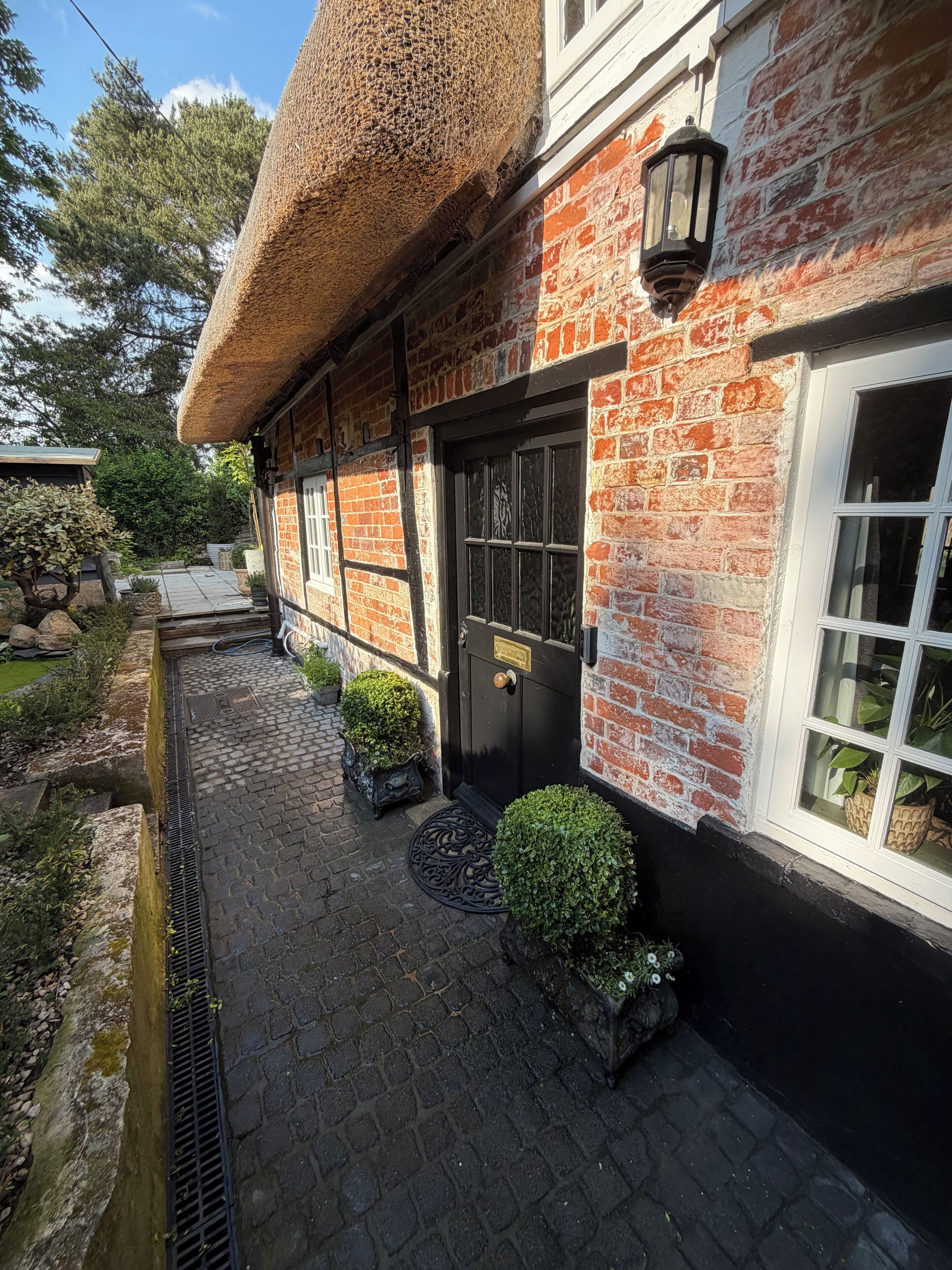A traditional brick building with a thatched roof, a black door, and a window with a white frame.. “A charming retreat with a story to tell”