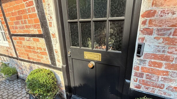 Uma porta preta com uma placa de latão, uma janela e um pequeno chamador de latão.
