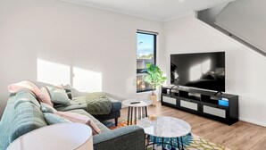 En moderne stue med en hjørnesofa, et fladskærms-tv, et lille rundt bord og en potteplante.