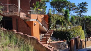 A multi-level building with outdoor stairs, a brick facade, and surrounding greenery. - Beautiful villa with all comforts, peace and quiet (Lloret de Mar)