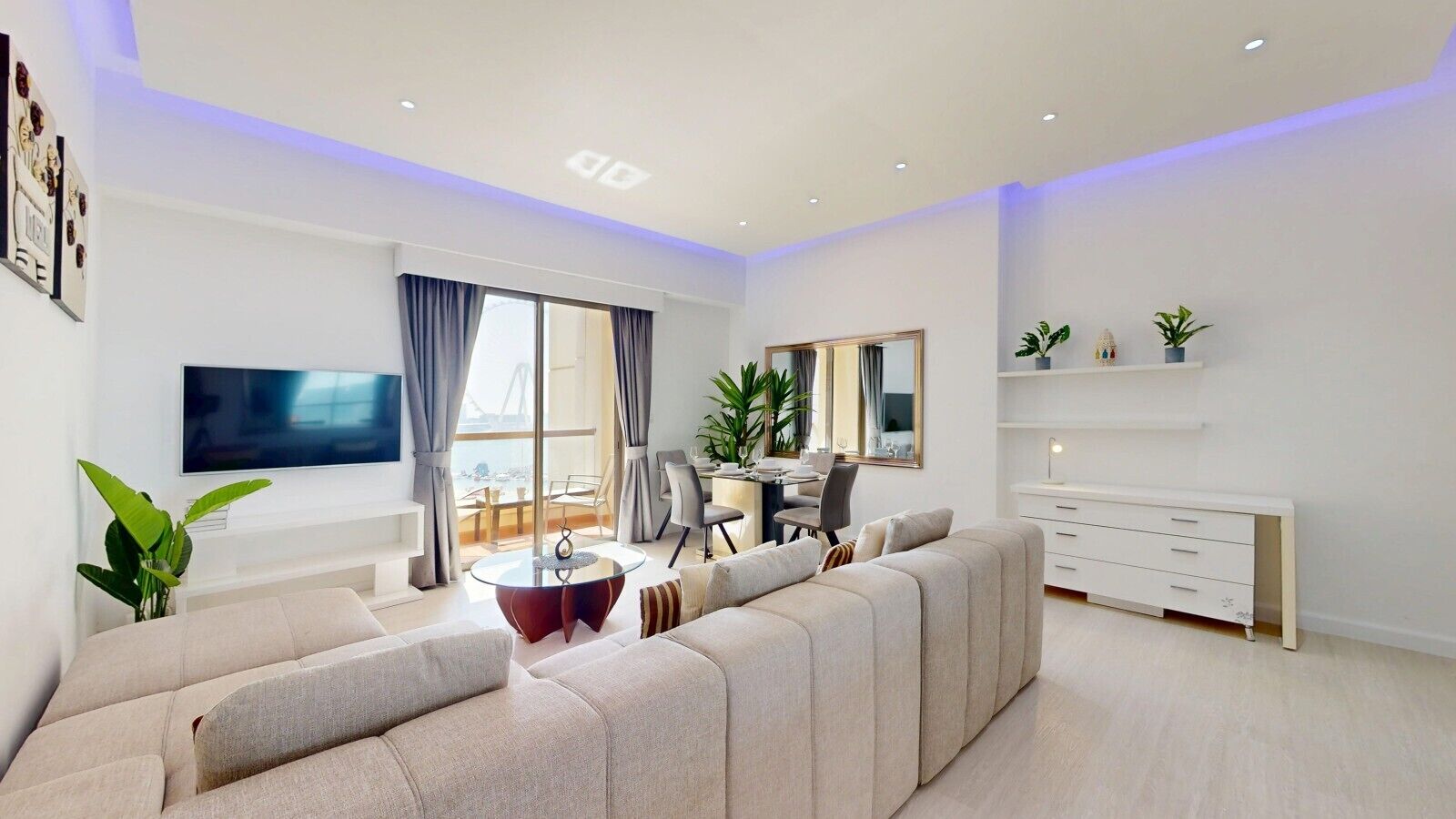 Un salon moderne avec un grand canapé, un coin repas, un téléviseur et une vue sur la mer.