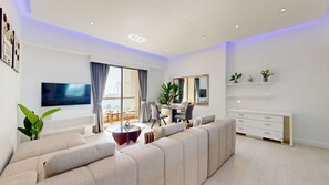 Ein modernes Wohnzimmer mit einer großen Couch, einem Essbereich, einem Fernseher und Blick auf das Meer.