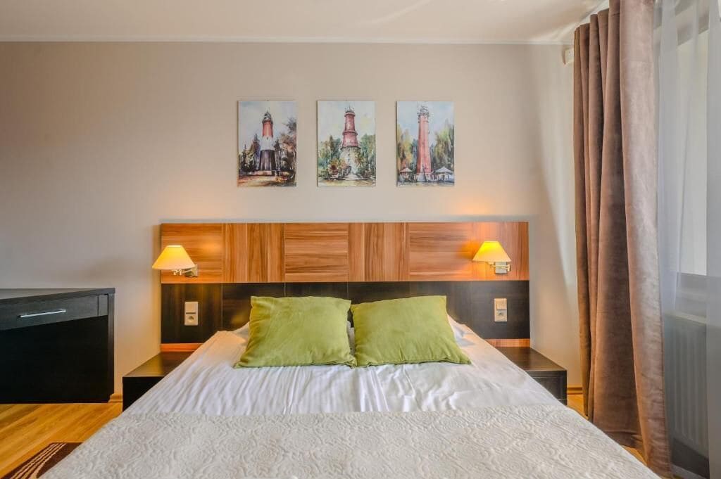 Habitación de hotel con una cama, dos lámparas de noche, un cabecero de madera y tres cuadros en la pared.