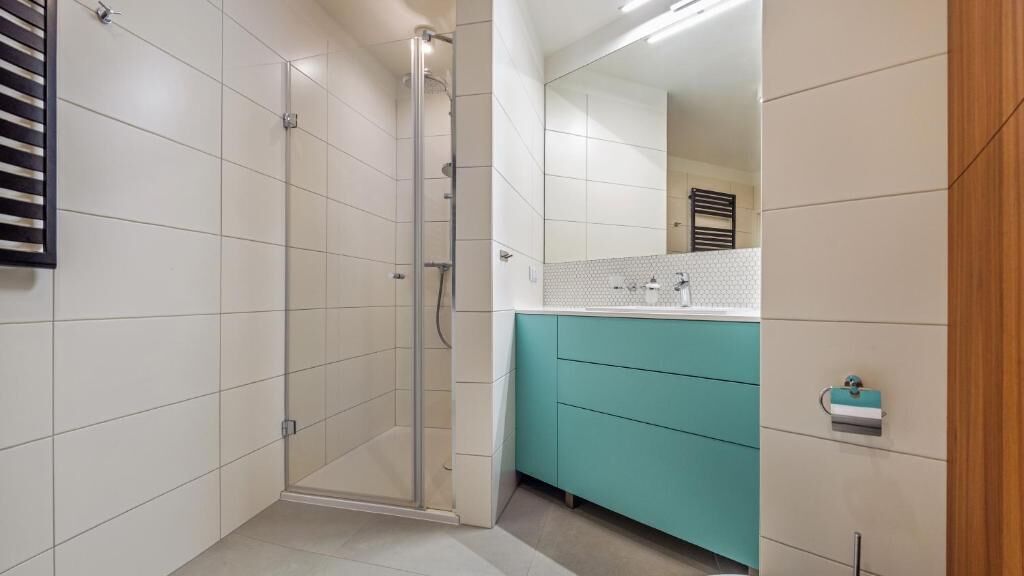 Une salle de bain moderne avec une douche à l’italienne en verre, un lavabo doté d’un plan de toilette blanc et un meuble-lavabo de couleur turquoise.