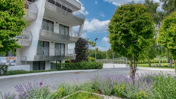 A modern building with balconies, surrounded by greenery and a paved area.