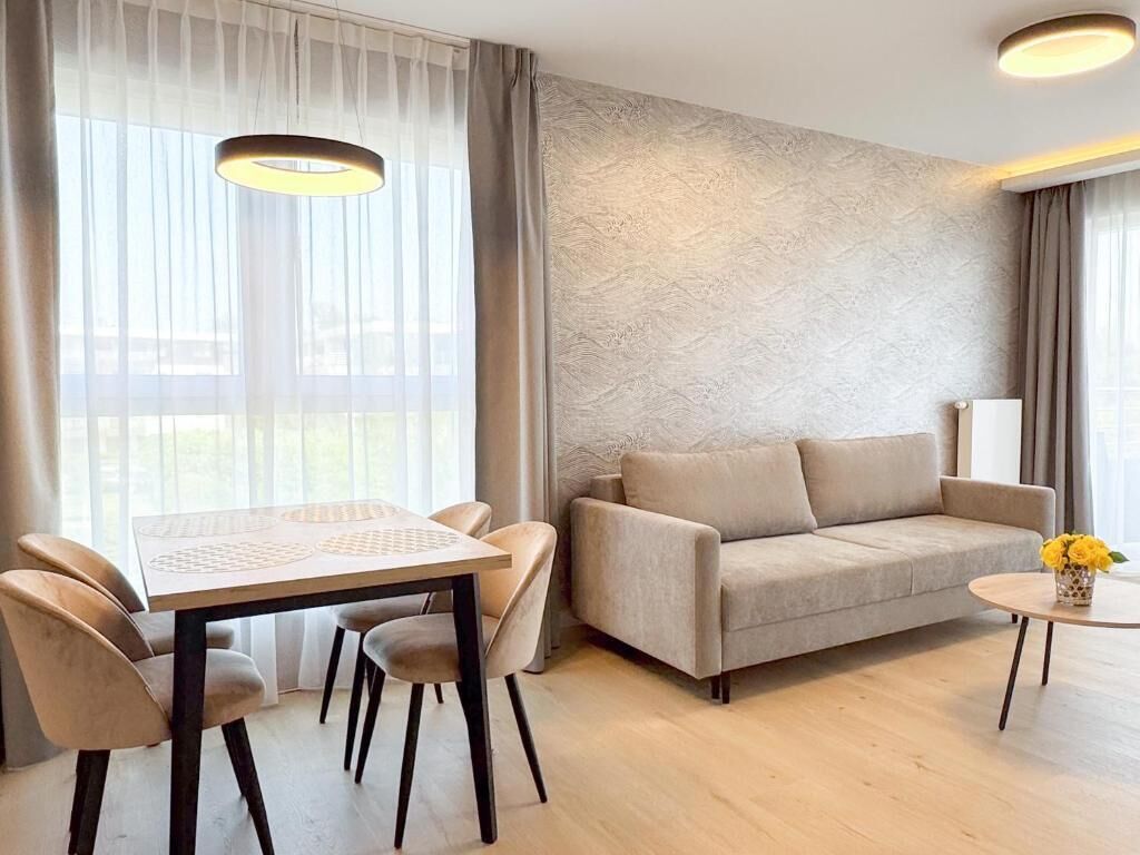A modern living room with a sofa, a dining table with chairs, and a small round table with a vase of flowers.
