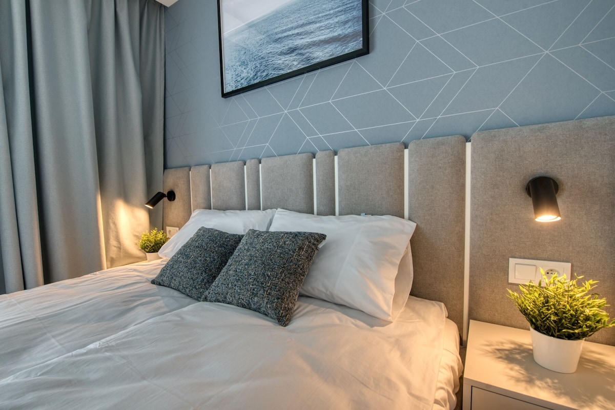 Una camera d'hotel moderna con un letto rifatto con cura, una parete con motivo geometrico e un quadro appeso sopra il letto.