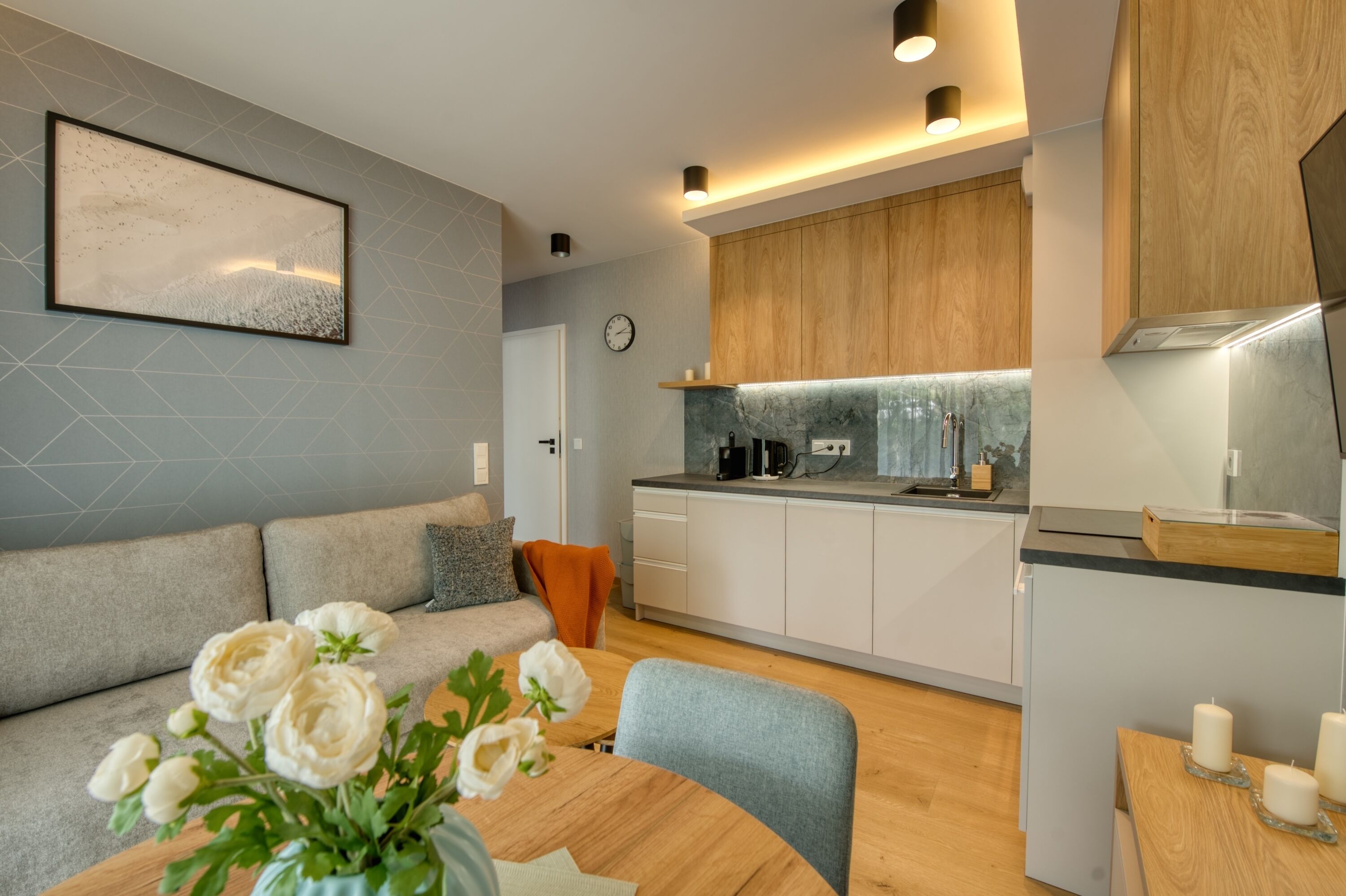 A modern kitchen with wooden cabinets, a marble backsplash, and a dining area with a table and chairs.