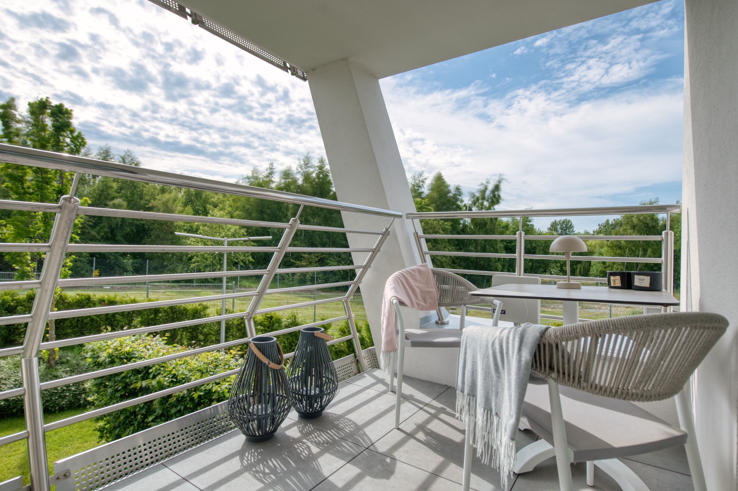 A balcony with a view of a park, a table with chairs, and a hanging chair.