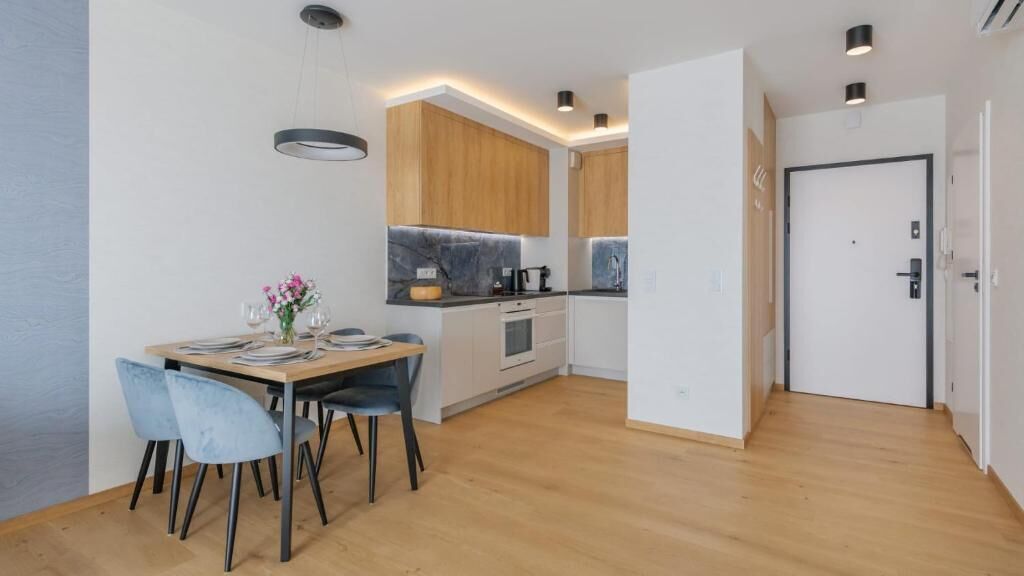 Una cocina moderna con armarios de madera, una mesa de comedor con sillas y una puerta que da a otra habitación.