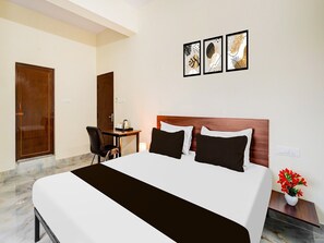 A hotel room with a bed, a desk, a chair, and a wall-mounted artwork. - Deluxe Hennur Prakruthi Layout Bangalore (Bengaluru)