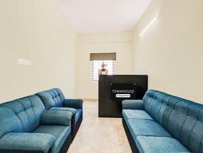 A reception area with two blue sofas, a black reception desk, and a window with blinds. - Deluxe Hennur Prakruthi Layout Bangalore (Bengaluru)