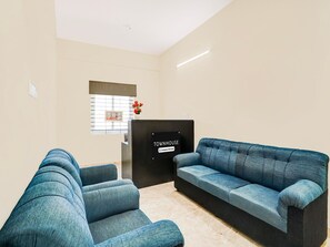 A reception area with a sign reading 'TOWNHOUSE,' two blue sofas, a small table, and a window with blinds. - Deluxe Hennur Prakruthi Layout Bangalore (Bengaluru)