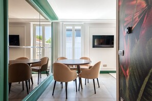 Ein modernes Zimmer mit einem runden Tisch und Stühlen, einem Flachbildfernseher an der Wand und einem großen Fenster mit Vorhängen.