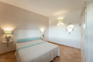 Ein Schlafzimmer mit einem Bett, Nachttischlampen, einem an der Wand befestigten Spiegel und einer Tür.