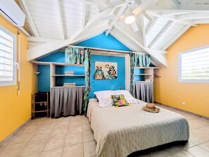 Un dormitorio con techo inclinado, una cama con cojín floral, un cuadro en la pared y estanterías empotradas.