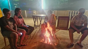 A group of people sitting around a campfire in an outdoor setting with chairs and tables. - Coorg Silent Stay - Homestay (Madikeri)