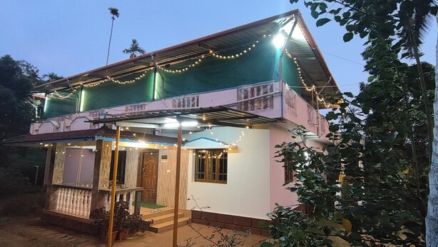 A two-story house with a balcony, a porch, and string lights. - Coorg Silent Stay - Homestay (Madikeri)